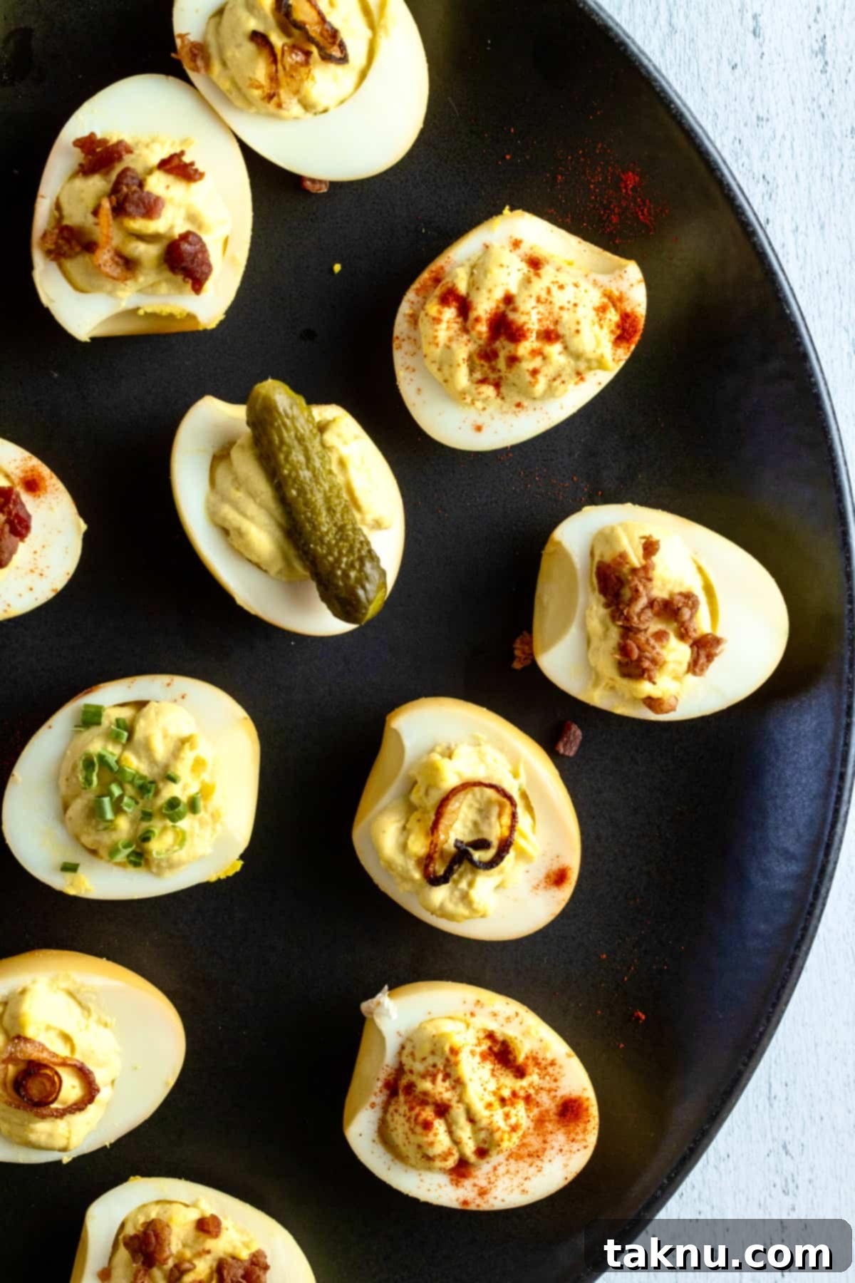 Smoky Deviled Delights 2 Deviled eggs on black platter with toppings such as pickles, bacon, paprika