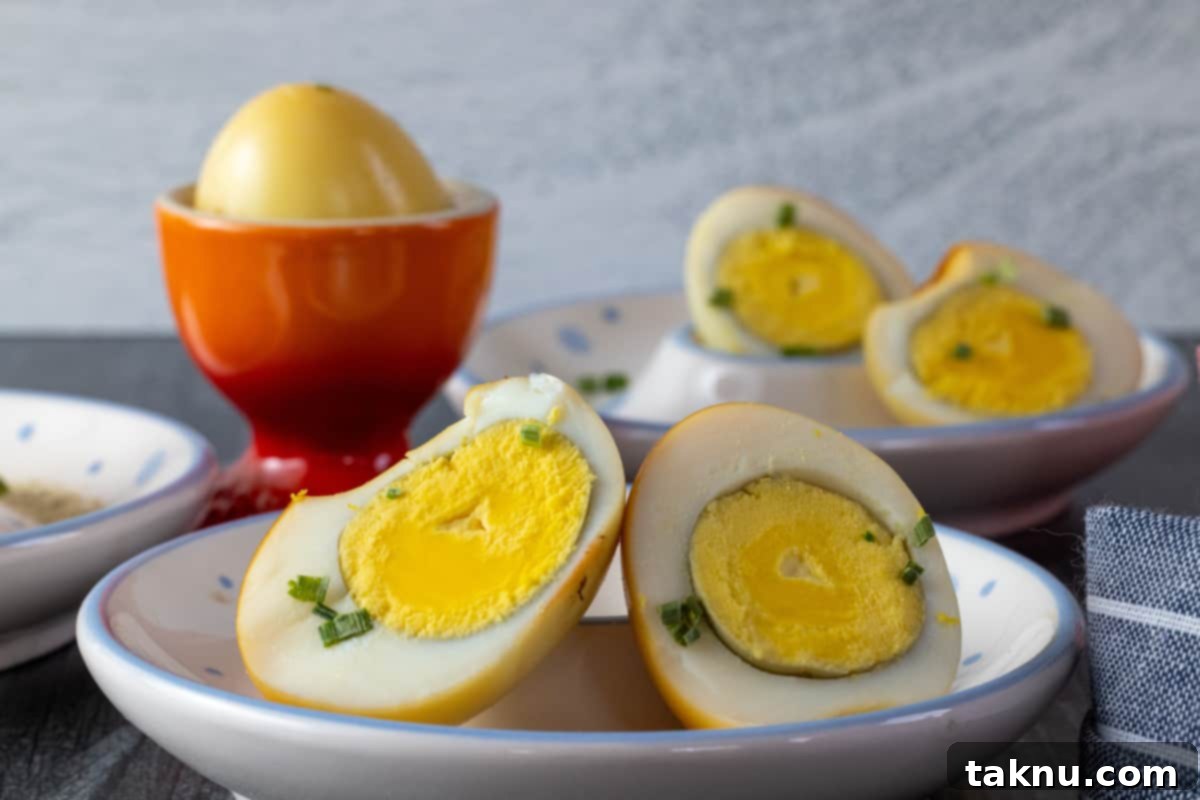 Boiled and smoked eggs cut in half on white dishes with a whole egg in a red dish, showcasing the golden color after smoking.