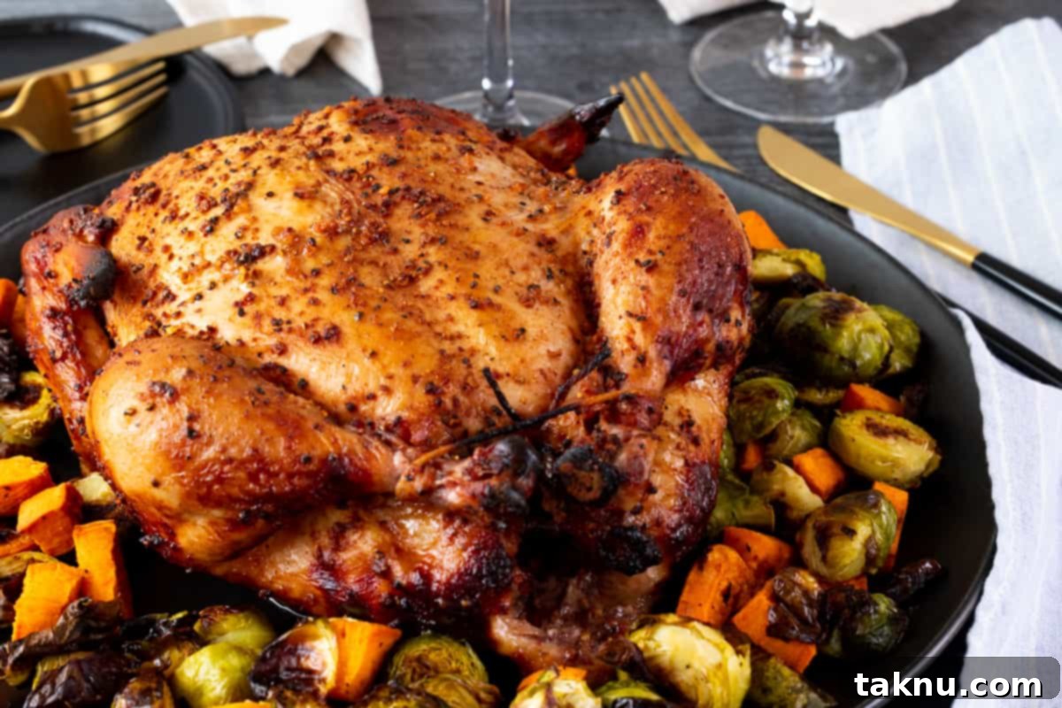 Traeger Smoked Buttermilk Chicken 7 A beautifully cooked whole chicken on a dark platter, surrounded by fresh vegetables and cutlery.