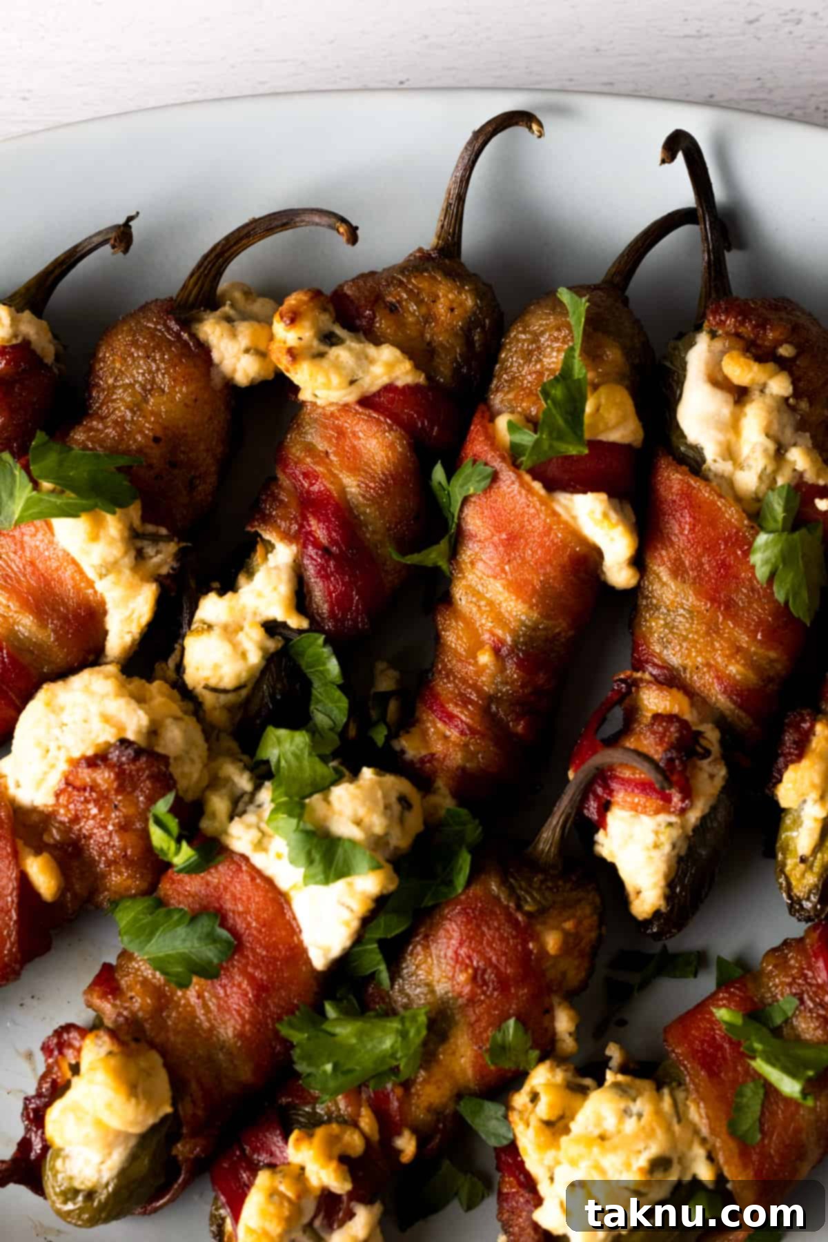 Fiery Smoked Jalapeño Bites 2 Bacon wrapped jalapeno poppers on white plate.