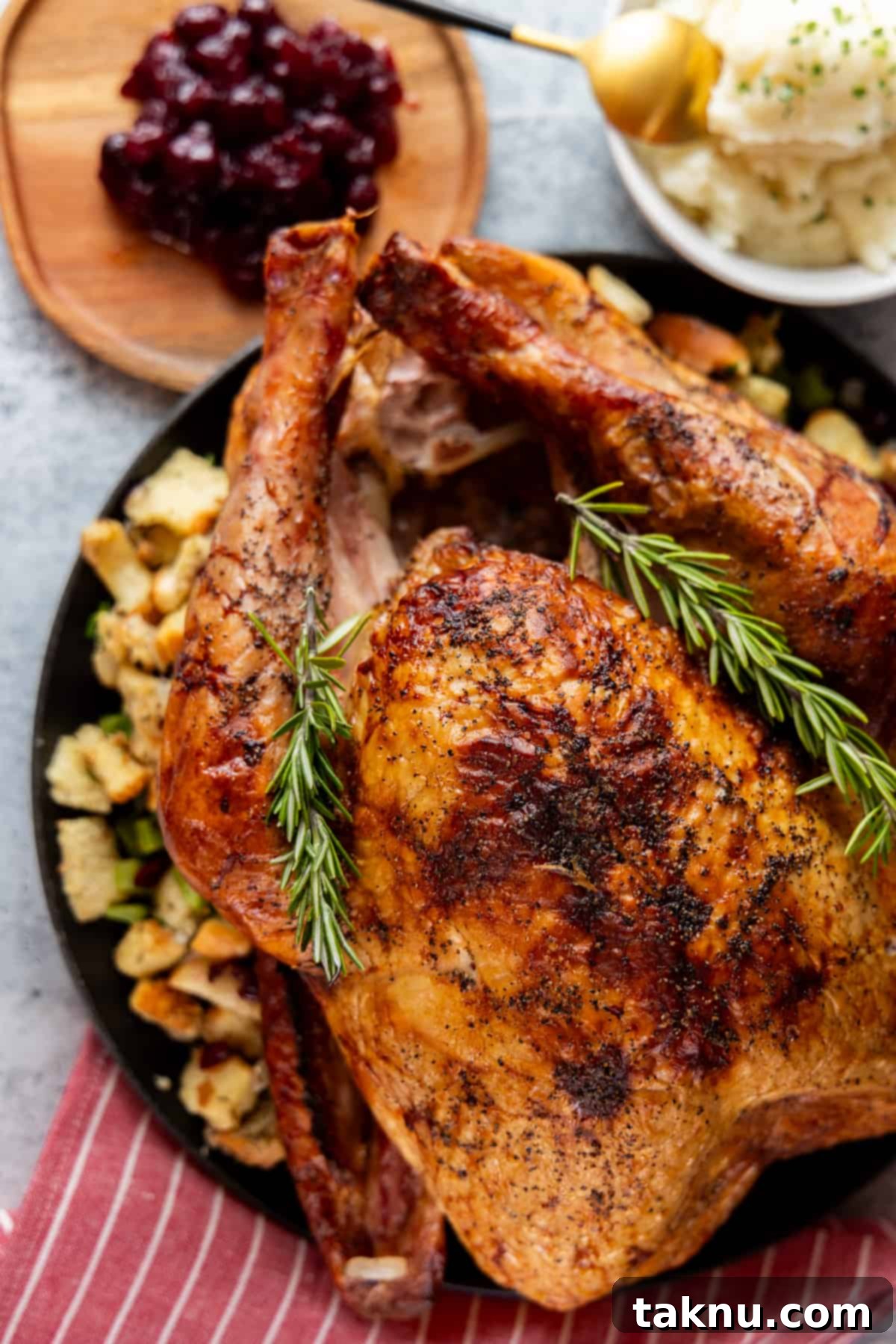 Turkey on black platter with potatoes and cranberry in the background. 