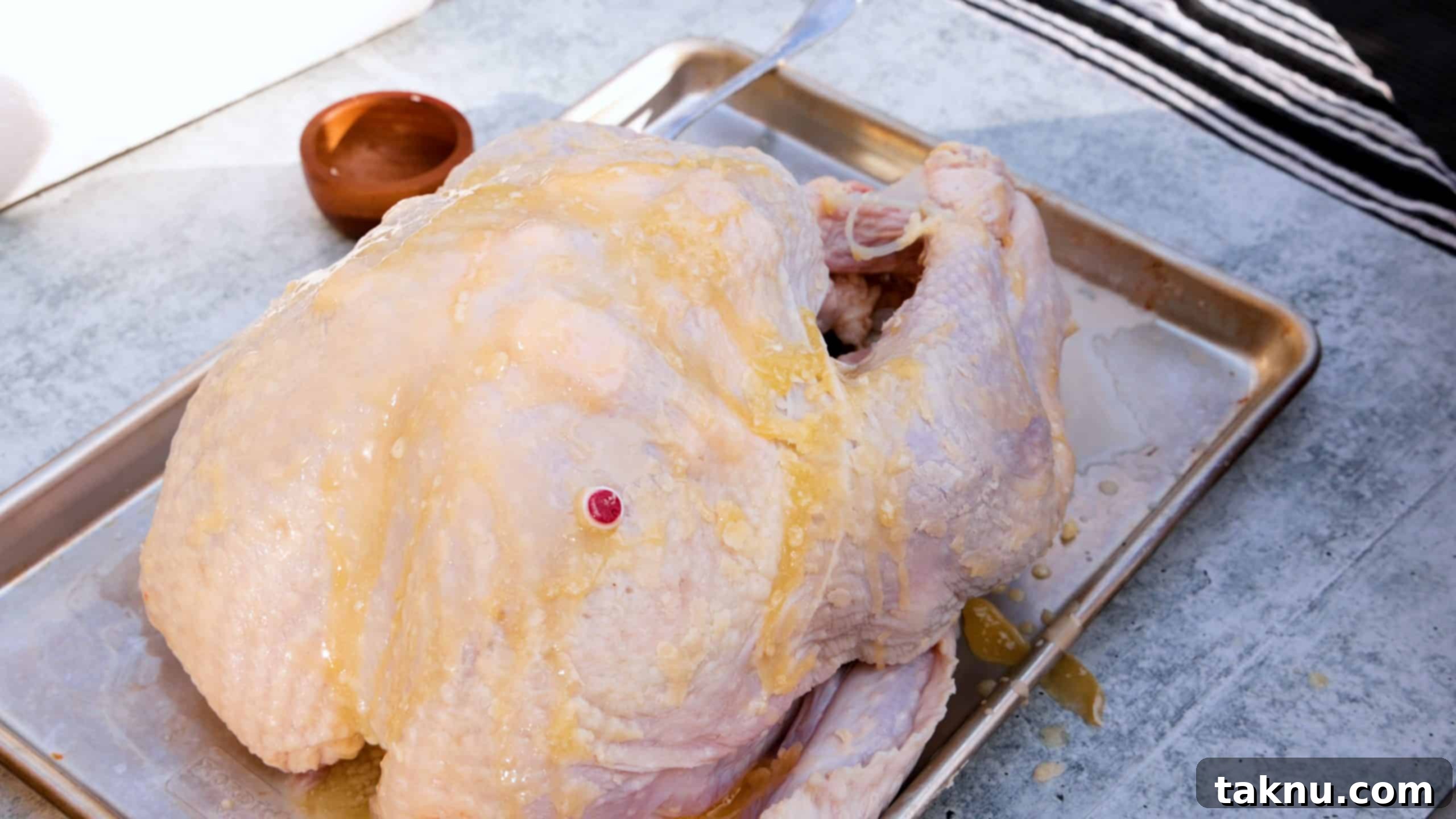 Uncooked raw turkey on baking sheet drizzled with melted butter.