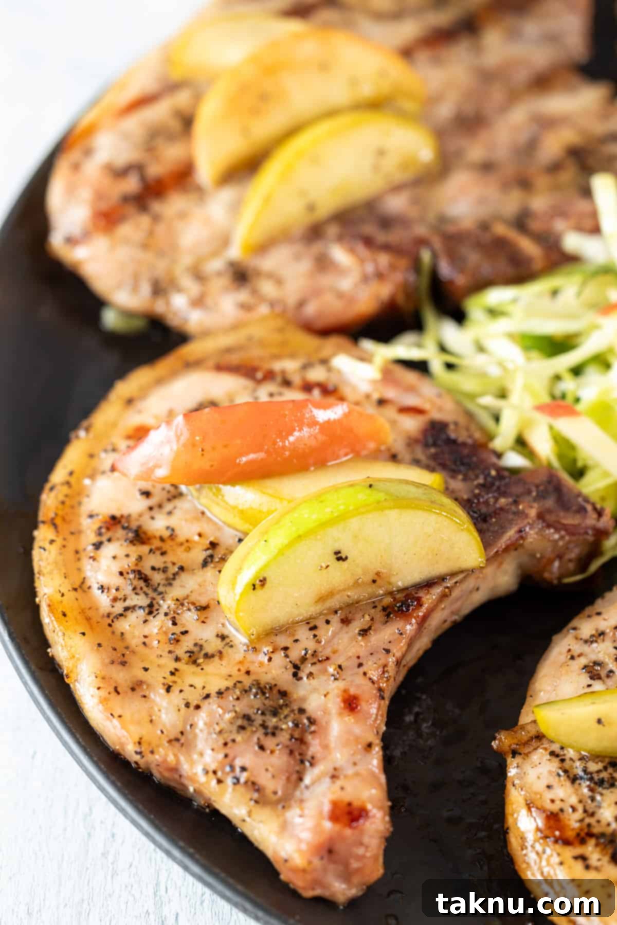 Smoky Pork Chops with Sweet Apple Glaze 2 Perfectly smoked pork chops on a black plate, garnished with fresh apple slices, ready to be served.