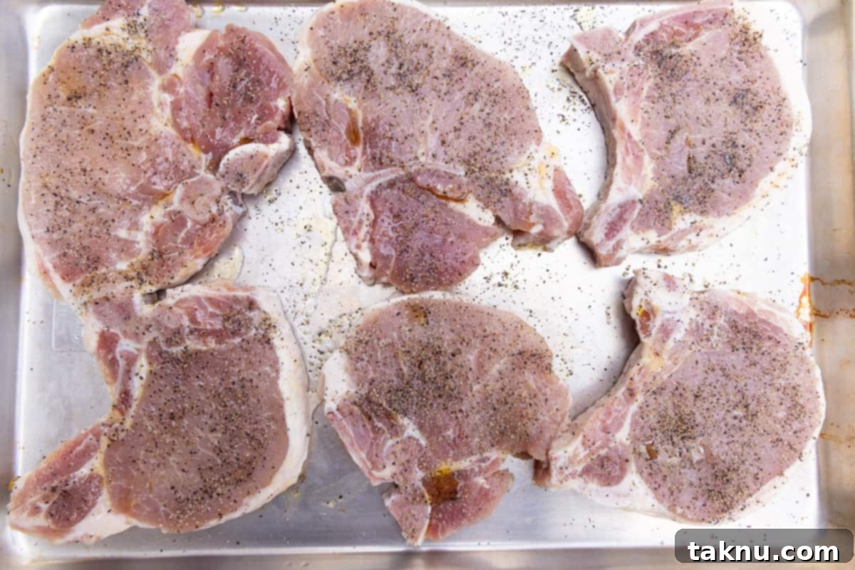 Smoky Pork Chops with Sweet Apple Glaze 5 Four seasoned pork chops resting on paper towels on a cutting board, ready for the grill, with fresh rosemary sprigs nearby.