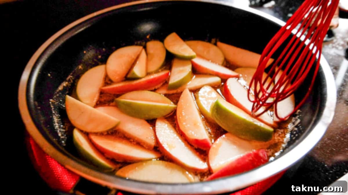 Smoky Pork Chops with Sweet Apple Glaze 6 Thinly sliced apples being gently stirred in a frying pan with a red whisk, coated in a sweet, shimmering glaze.