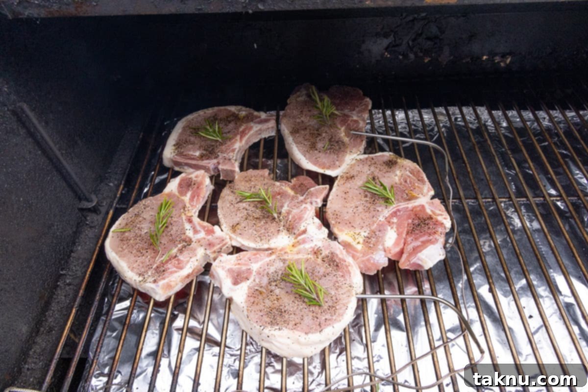 Smoky Pork Chops with Sweet Apple Glaze 7 Four bone-in pork chops smoking on grill grates, each topped with a fresh sprig of rosemary, emitting a fragrant aroma.