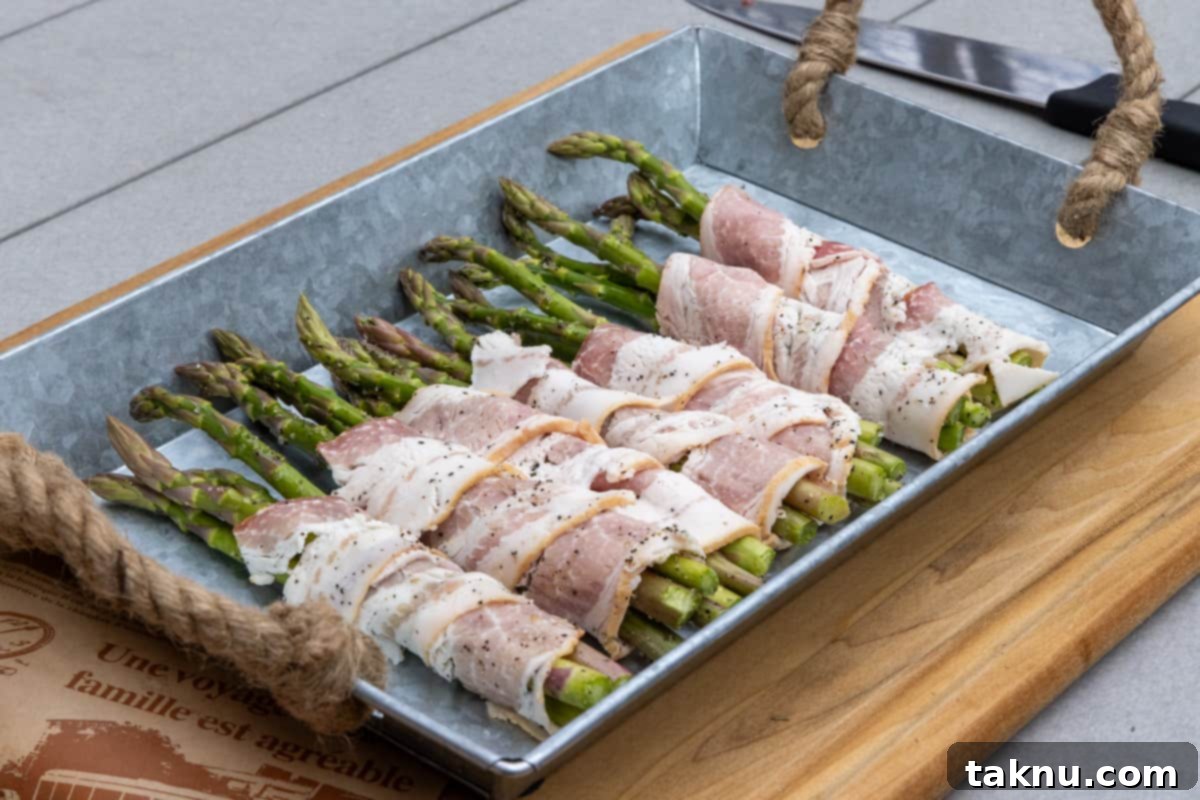 Smoked Bacon Wrapped Asparagus 5 Asparagus wrapped in bacon on tray atop a wood cutting board, ready to be grilled.