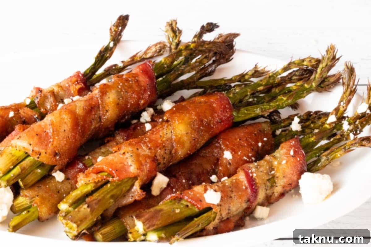 Smoked Bacon Wrapped Asparagus 7 Bacon wrapped around asparagus topped with blue cheese on white plate.