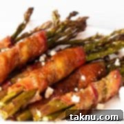 Sizzling Christmas BBQ Recipes 12 Bacon wrapped around asparagus topped with blue cheese on white plate.