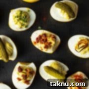 Sizzling Christmas BBQ Recipes 14 Deviled eggs on black platter with pickles, bacon, shallots, and paprika garnish.