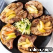 Sizzling Christmas BBQ Recipes 10 Five pork chops on a black plate topped with apples with a napkin and silverware beside plate.