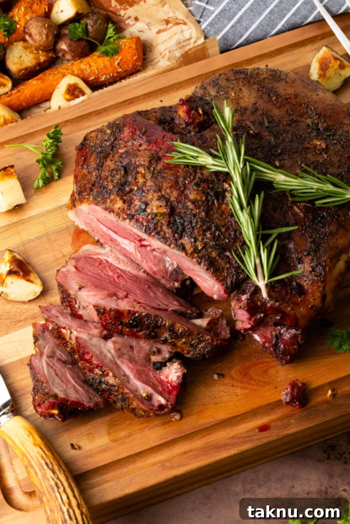Leg of lamb on cutting board with rosemary atop roast.