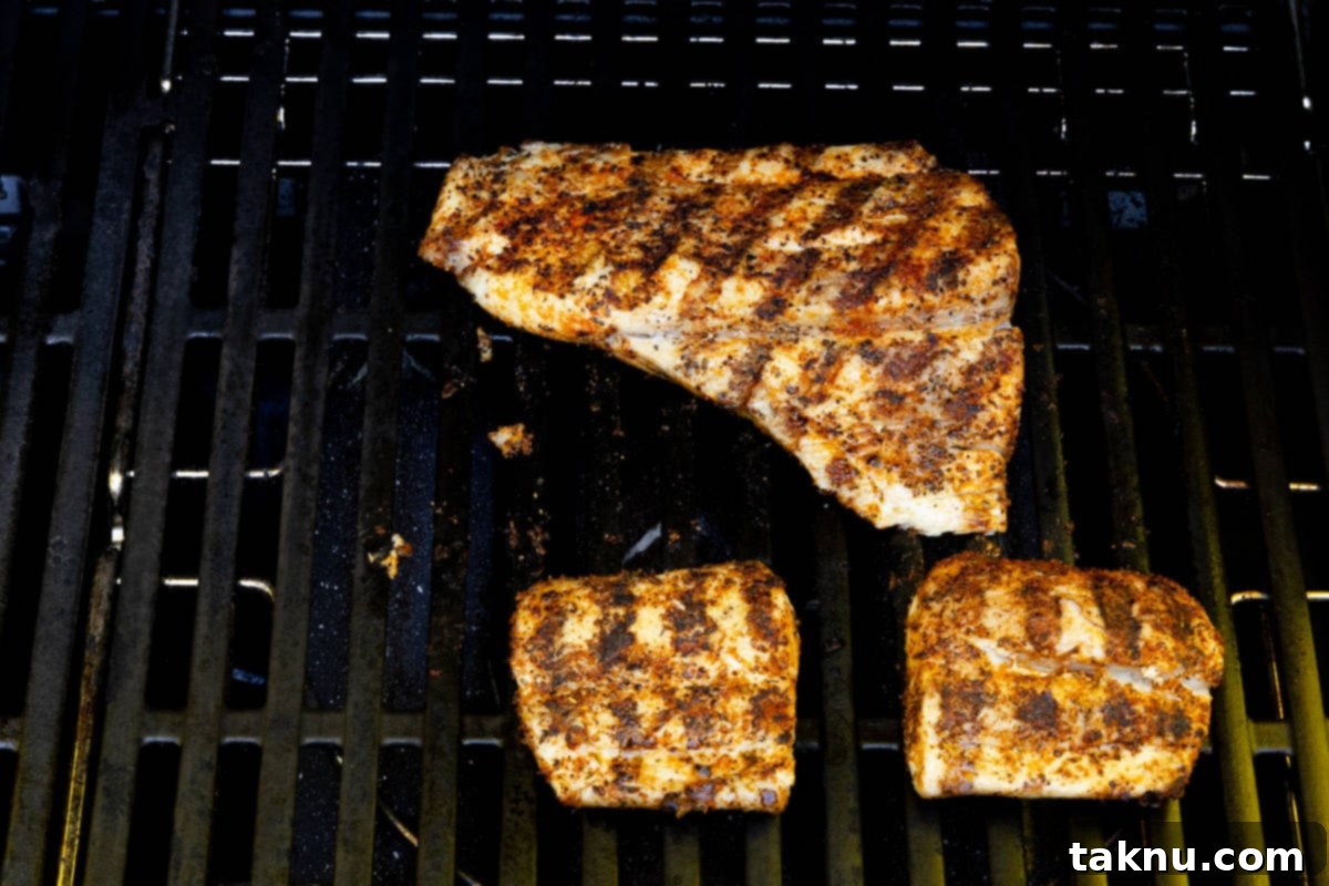 Three seasoned mahi mahi fillets cooking on hot grill grates.