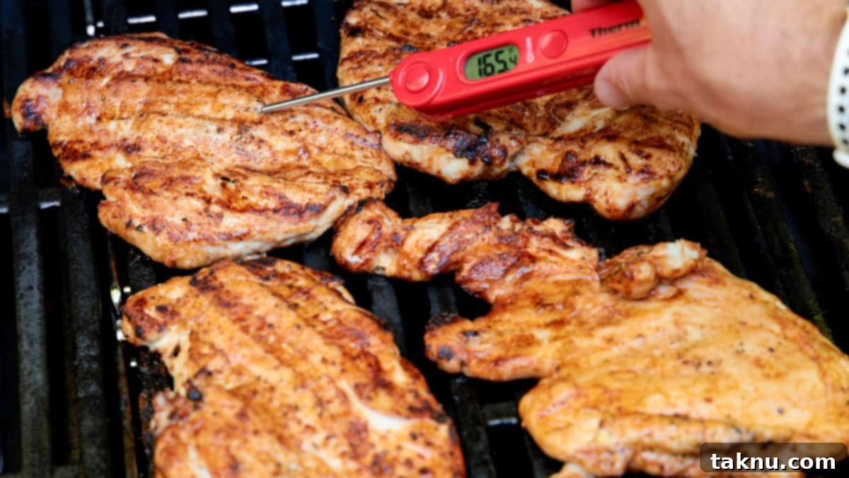 A digital meat thermometer inserted into a grilled chicken breast on the grill, displaying an internal temperature of 165 degrees Fahrenheit, indicating perfect doneness.