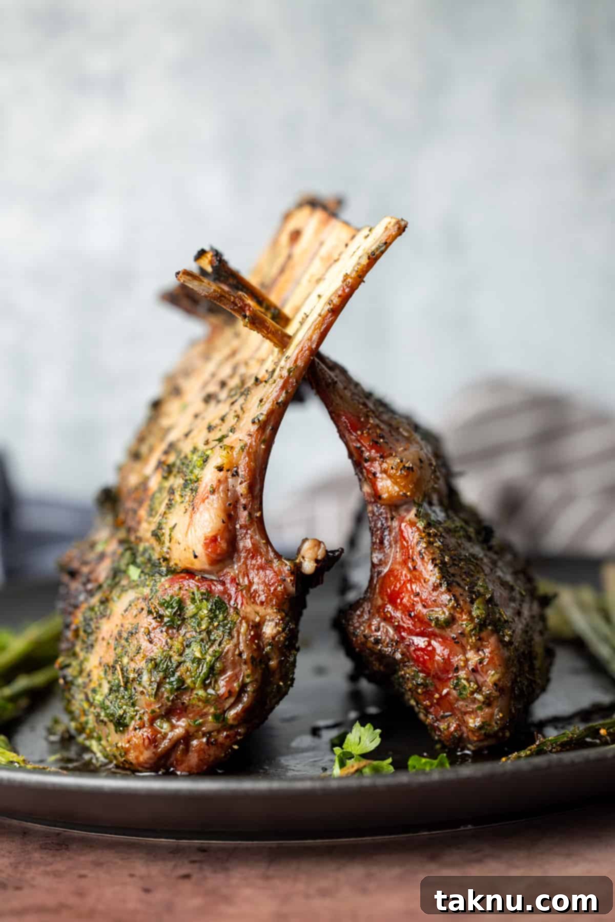 Two racks of lamb cooked on top of a black plate with white background, showcasing a perfect medium-rare doneness and golden crust.