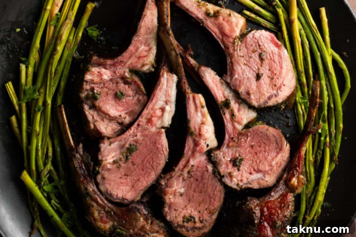 Five lamb chops beautifully arranged on a black platter, accompanied by grilled asparagus.