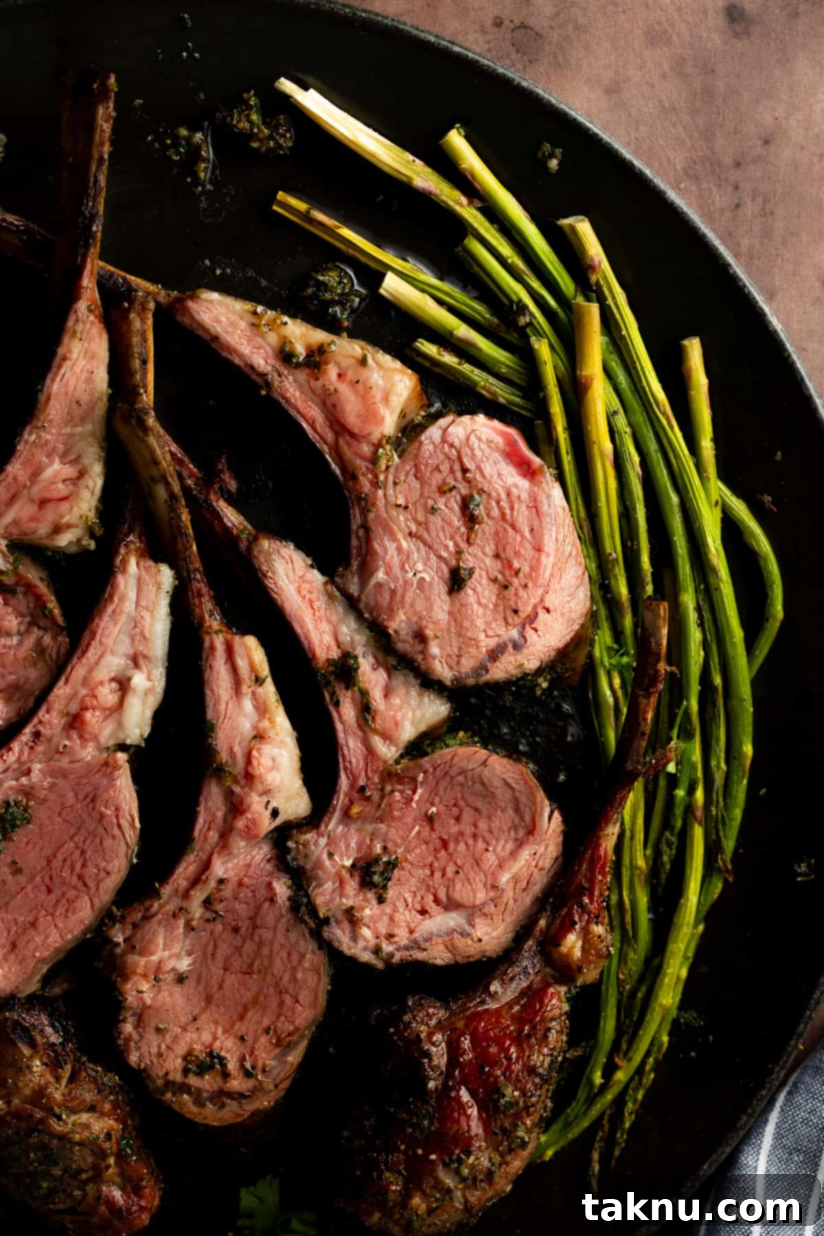 Beautifully cooked lamb chops presented on a sleek black plate, accompanied by a vibrant side of perfectly grilled asparagus, ready to be served.