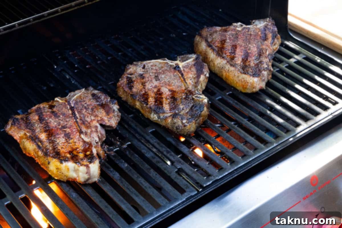 Three t bone steaks on grill cooking.