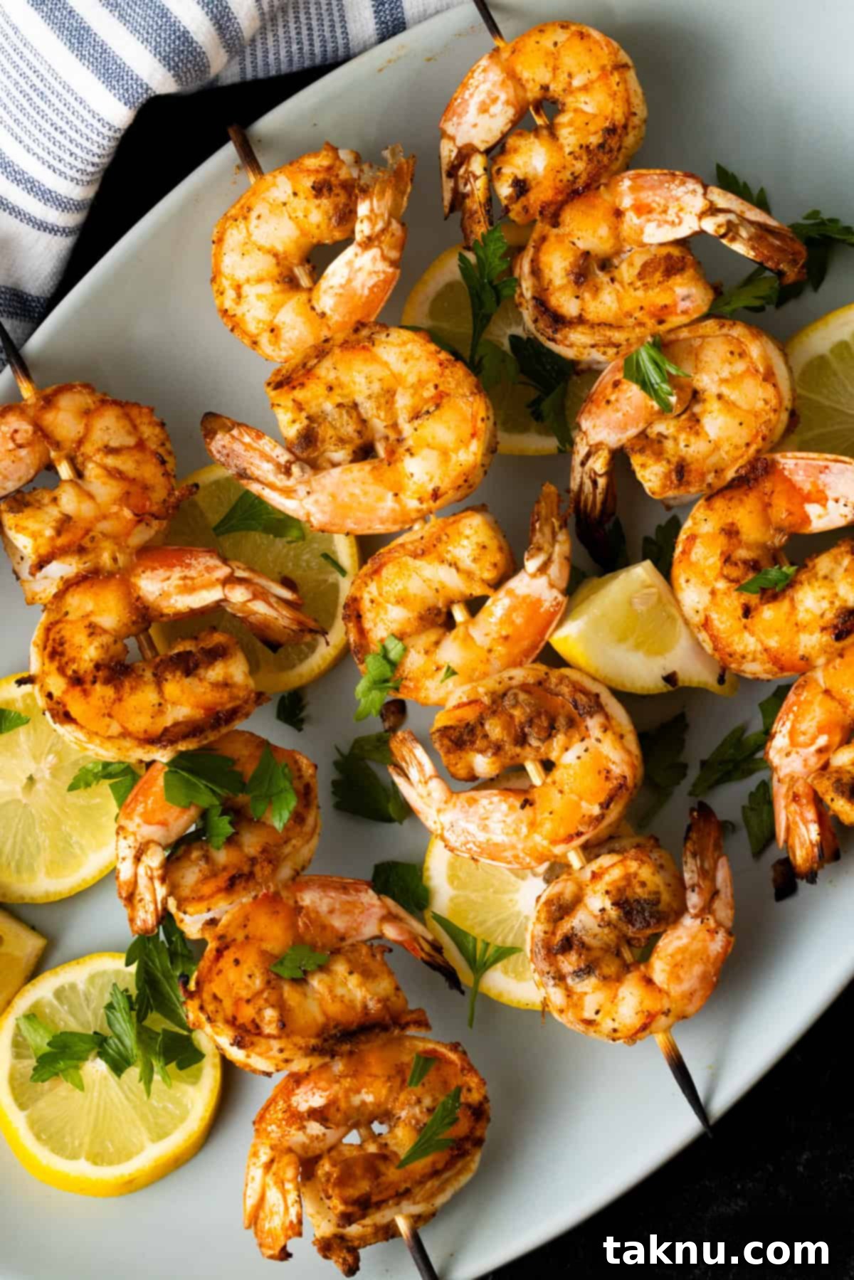 Grilled shrimp on wooden skewers atop a white plate garnished with lemon wedges and fresh parsley.
