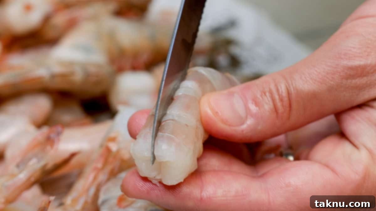 A hand using a sharp knife to carefully slice along the back of a shrimp, preparing it for deveining and butterflying.