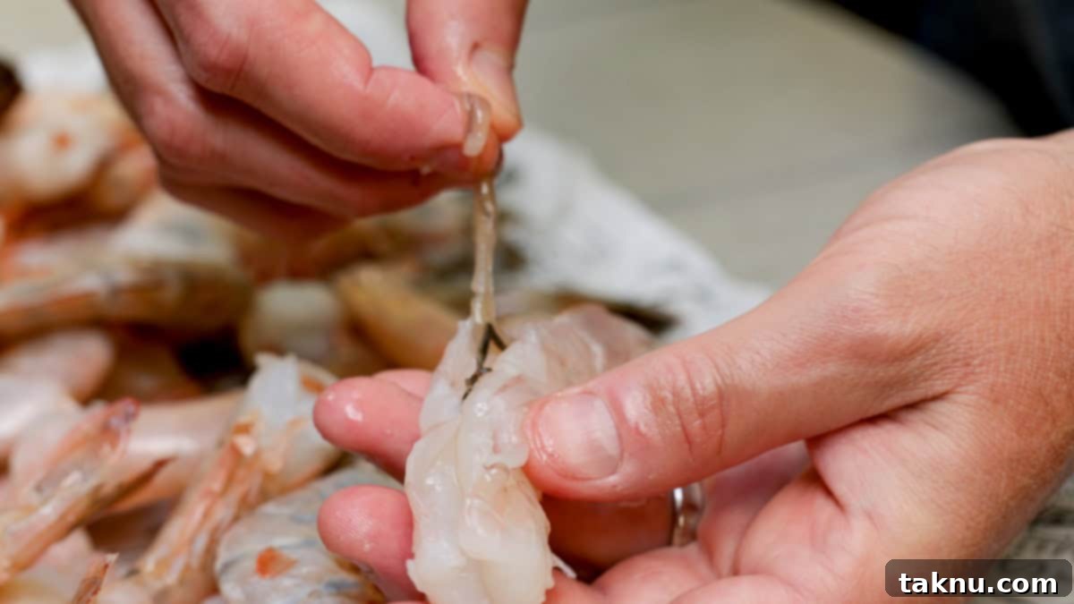 A close-up of a hand meticulously deveining a shrimp, removing the dark intestinal tract.
