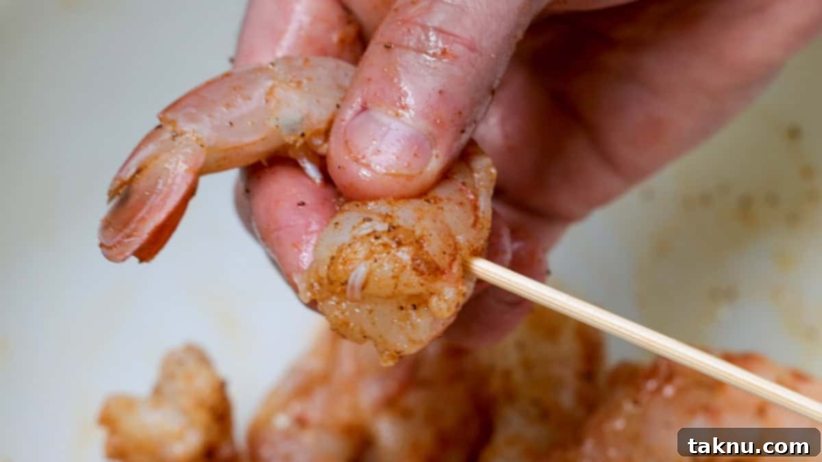 A hand meticulously placing seasoned shrimp onto a wooden skewer, preparing them for grilling.