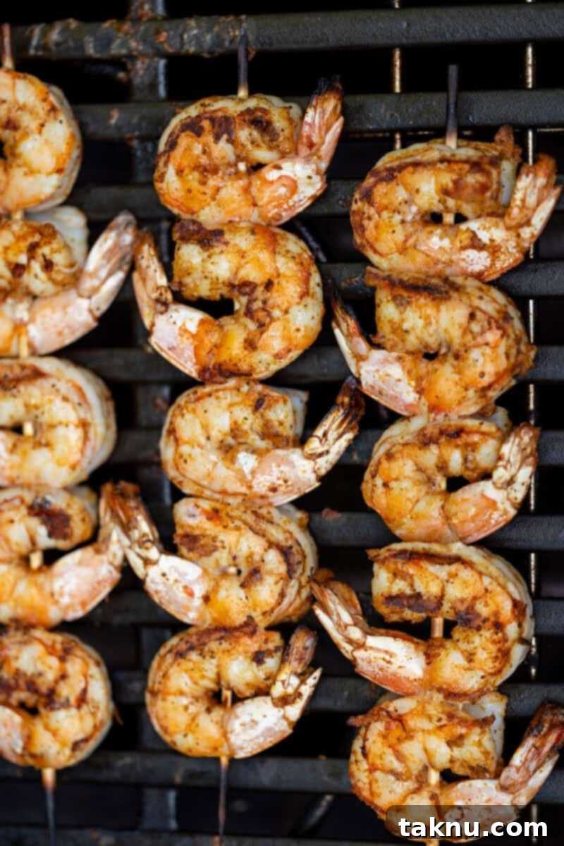 Three skewers of seasoned shrimp cooking directly on hot grill grates, close up.