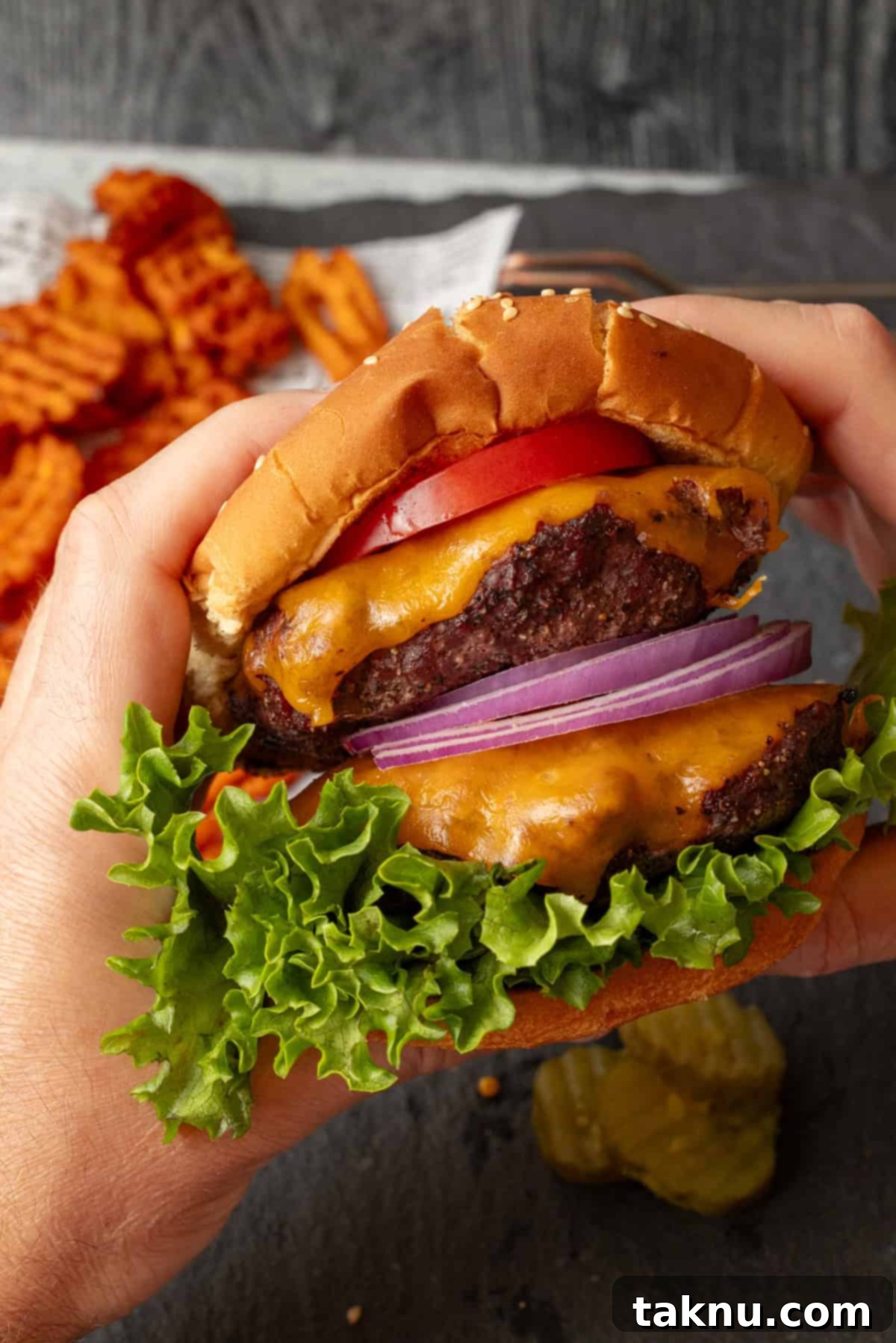 Bison burger with lettuce, onion, tomato, on a bun being held with two hands.