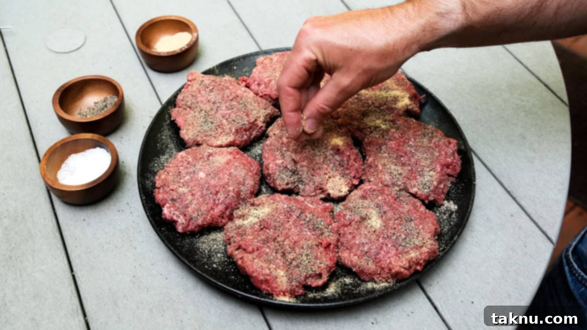 Seasoning a black plate of 7 bison burgers with salt, pepper, garlic by hand.
