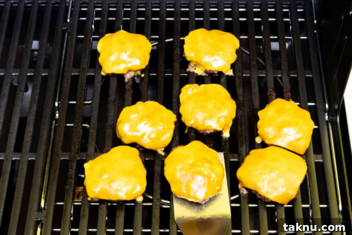 Eight bison burgers on grill covered in cheese.