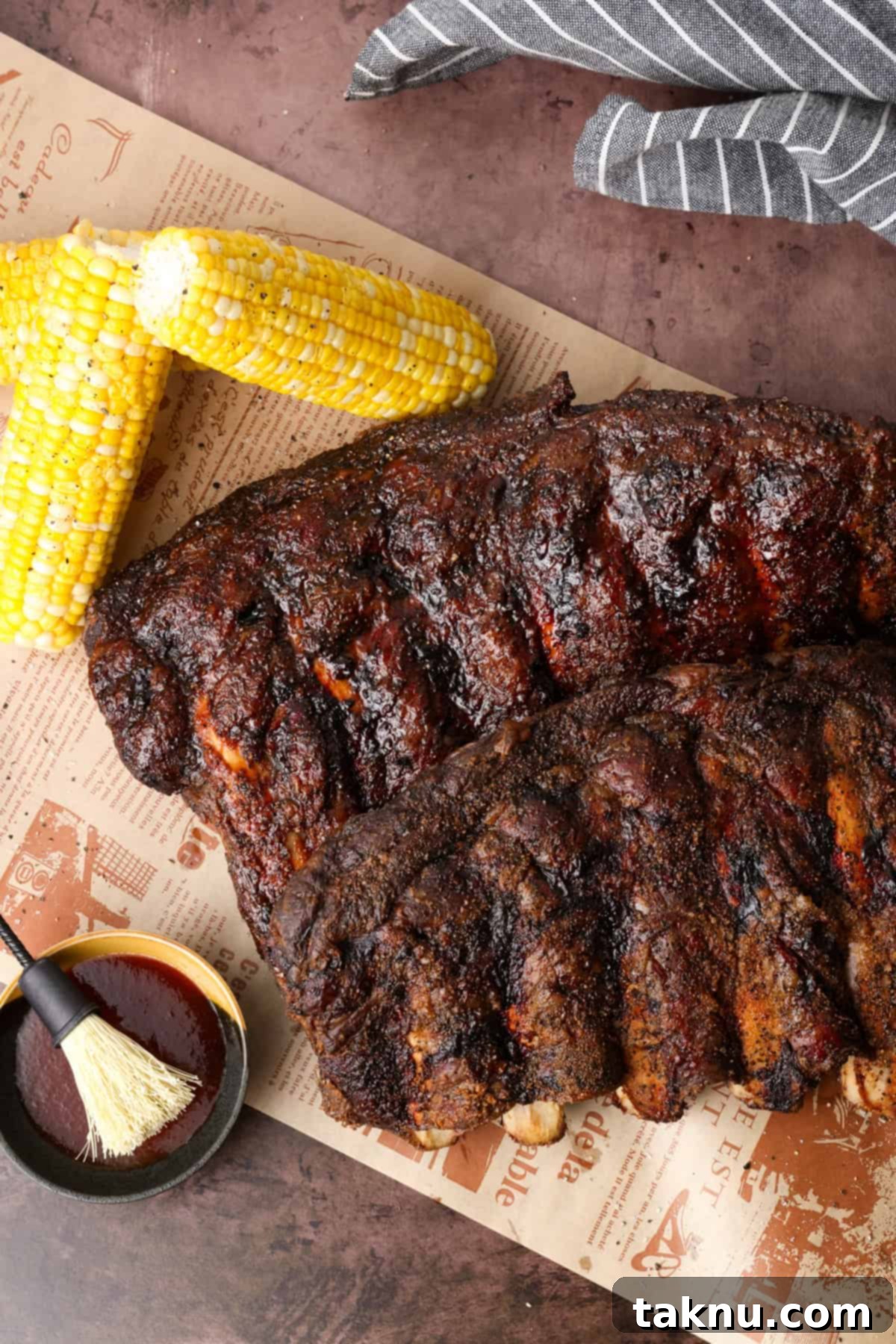 Two racks of beef ribs on cutting board with two corn on the cobs.