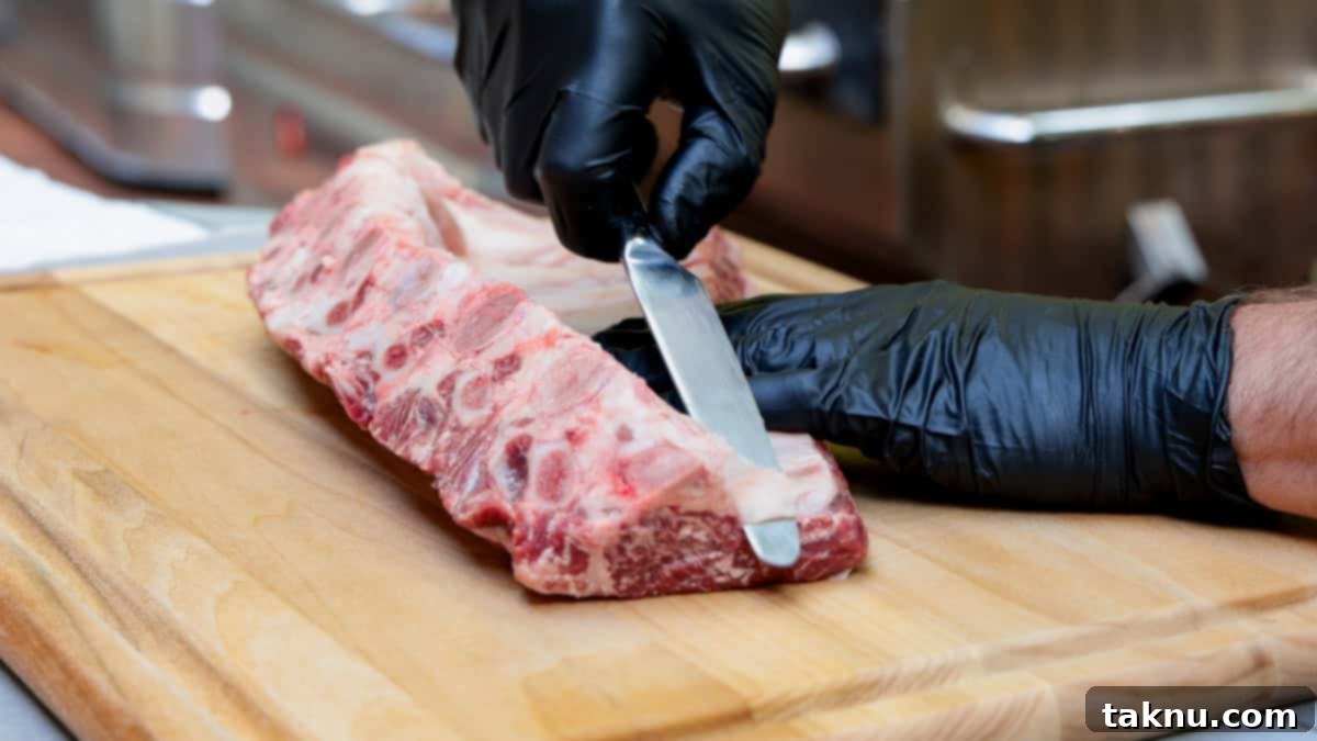 Using a knife to remove the membrane from rack of beef ribs atop a cutting board.