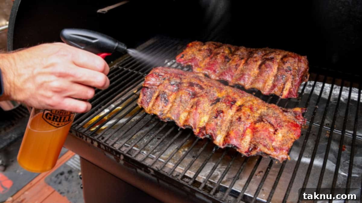 Spraying two racks of beef ribs on grill with apple cider vinegar out of spray bottle.