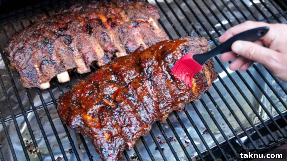Brushing BBQ sauce on two racks of beef ribs on grill.