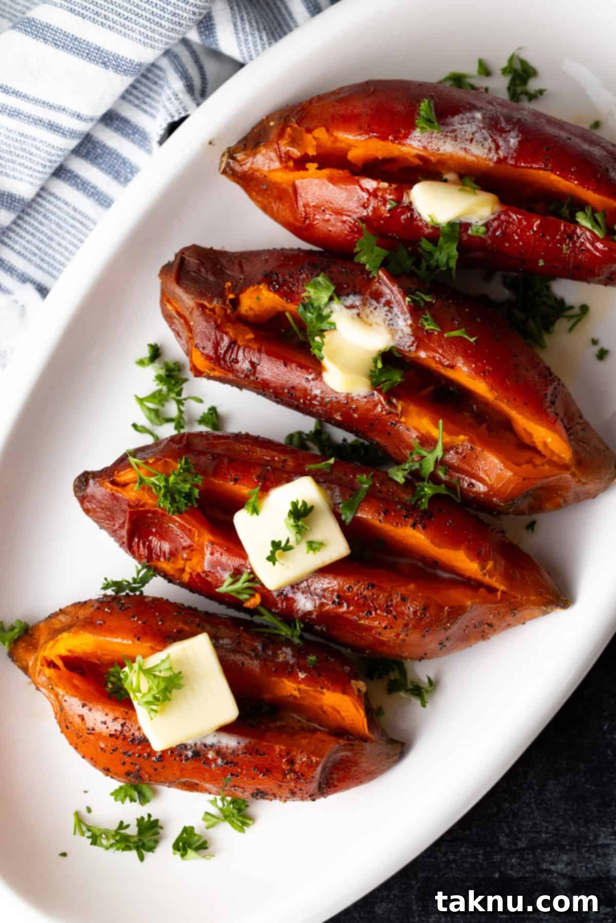 Four grilled sweet potatoes topped with butter on white plate.
