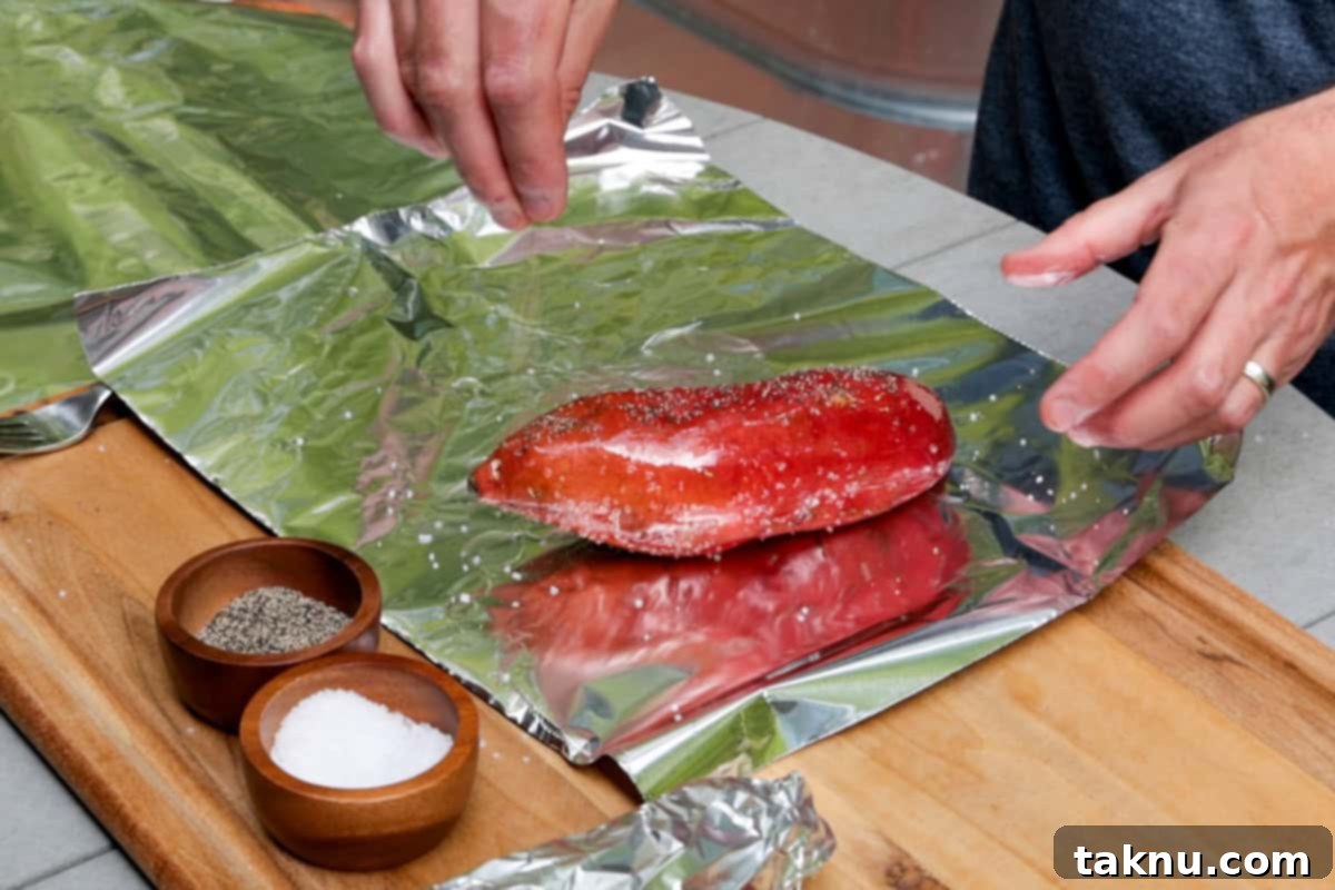 Potato on aluminum foil being seasoned with salt and pepper by hand.