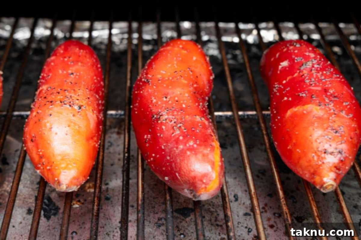 Three sweet potatoes cooking on grill.