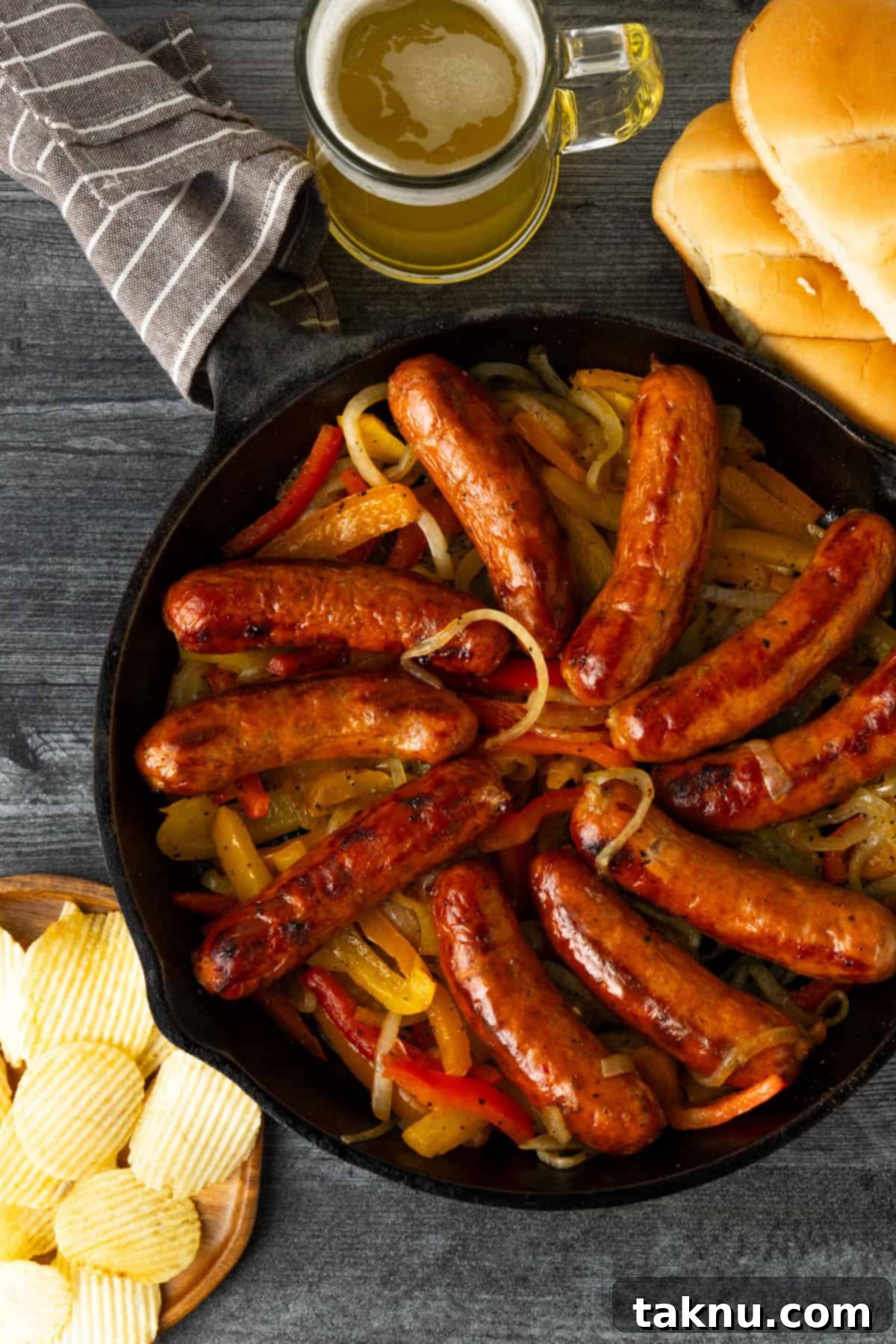 Savory Sausage and Roasted Peppers 2 Grilled sausages atop onions and peppers in a cast iron surrounded by potato chips, beer, and hot dog buns.