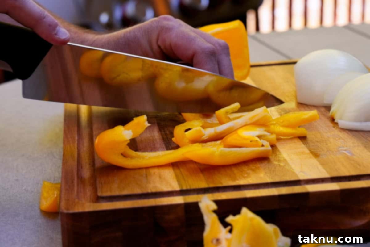 Savory Sausage and Roasted Peppers 4 Slicing yellow bell pepper on wood cutting board with large knife.