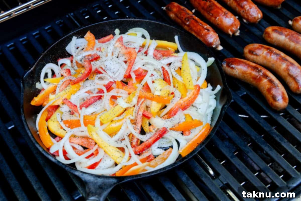 Savory Sausage and Roasted Peppers 7 Cast iron with sliced onions and peppers on a grill with several sausages.