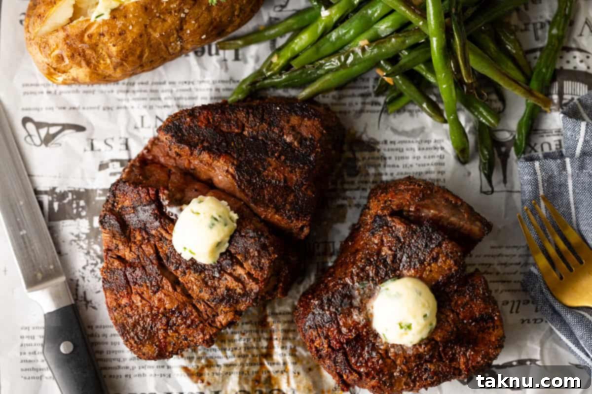 Two perfectly grilled filet mignon steaks topped with melting butter, served alongside a fluffy baked potato and vibrant green beans on a rustic newspaper spread.