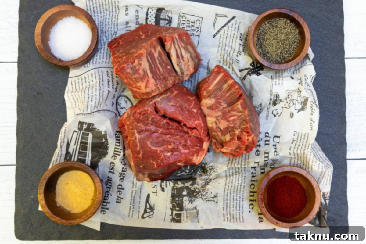 A close-up shot of raw filet mignon steaks resting on newspaper, surrounded by small wooden bowls containing the simple yet potent seasonings: sea salt, black pepper, smoked paprika, and garlic powder.