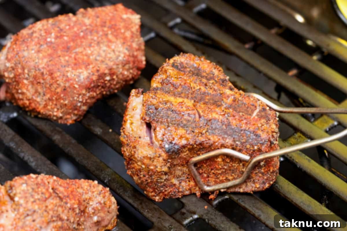 Metal tongs carefully turning filet mignon steaks on a hot grill, showing excellent sear marks as they cook to perfection.