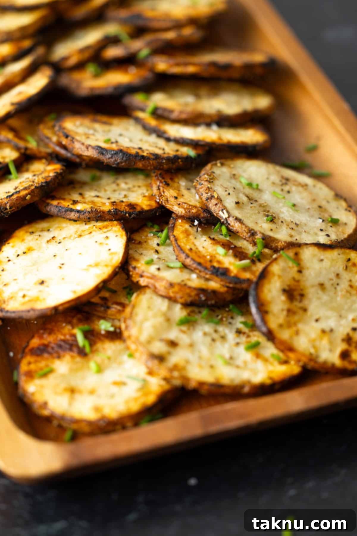 Grilled sliced potatoes on a wooden serving board, garnished with fresh herbs and lemon wedges.