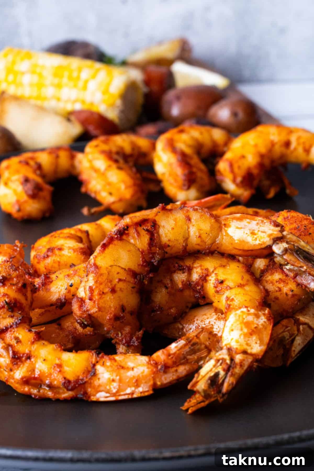 Succulent Smoked Shrimp 14 Smoked shrimp elegantly arranged on a black plate, with grilled corn on the cob visible in the background, creating an inviting summer scene.