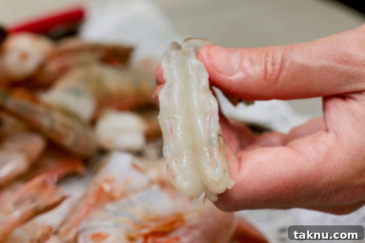 Succulent Smoked Shrimp 6 A deveined and thoroughly rinsed shrimp being held, with a clean plate of other prepared shrimp in the background, ready for seasoning.