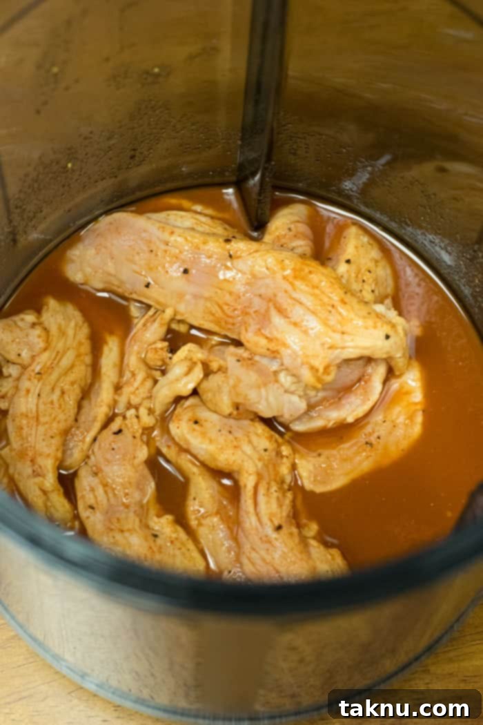 Raw turkey jerky strips steeping in a rich, dark Smokey Cajun marinade, allowing the powerful spices and flavors to fully penetrate the meat before dehydration.