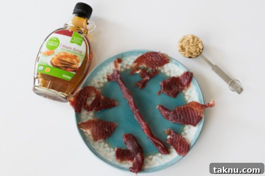 Sweet Maple Pork Jerky on plate with bottle of maple syrup and tablespoon of brown sugar