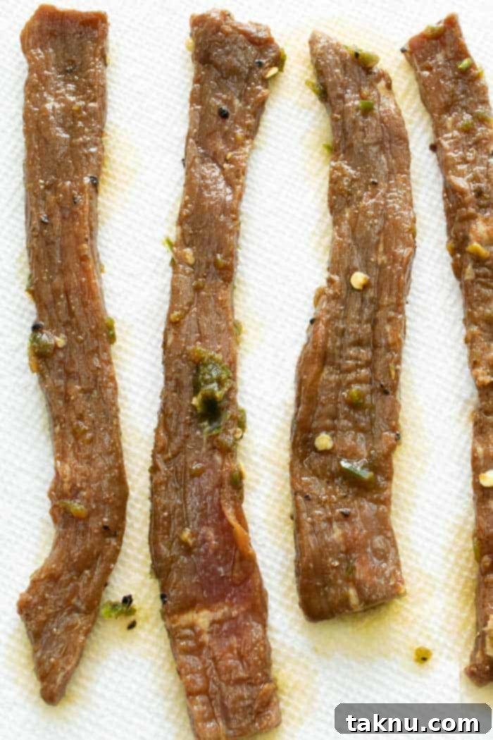 Jalapeño beef jerky strips laid out on paper towels, being patted dry to remove excess moisture and promote even drying