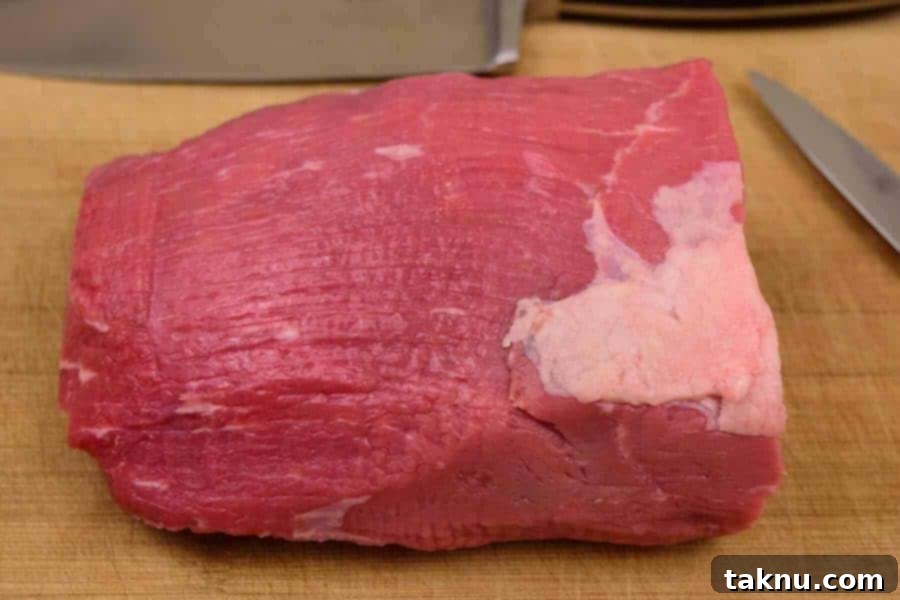Beef Eye of Round Roast being meticulously trimmed of all visible fat on a cutting board, essential for long-lasting jerky